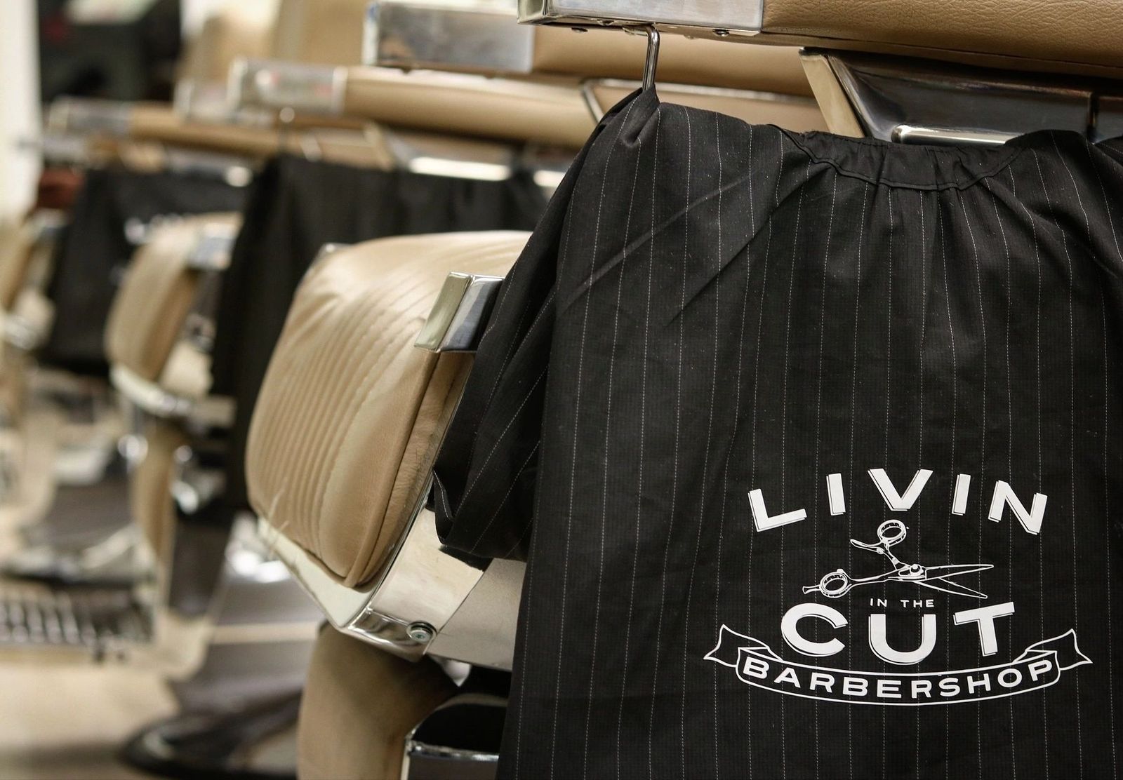 A pinstriped Livin In The Cut cape hanging over the back of a barber chair.