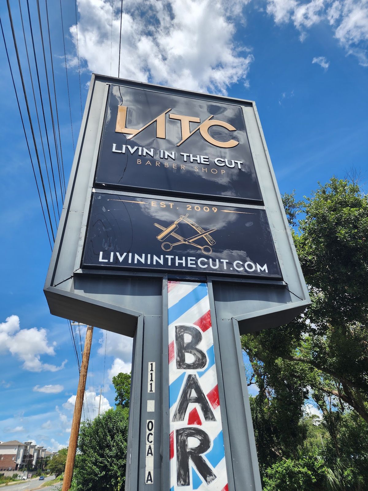 The Livin In The Cut road sign on N. Ocala Rd, gold lettering on black above a painted barber pole.